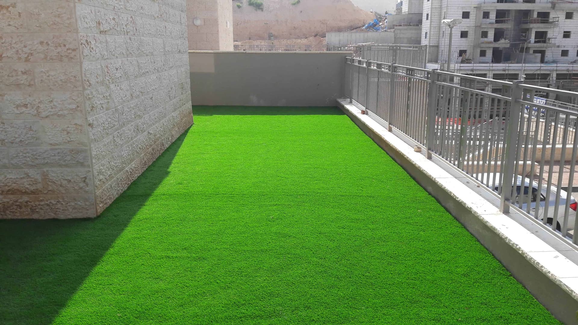 מרפסת רחבה בעיר עם דשא סינטטי ירוק לצד מעקה מתכת.